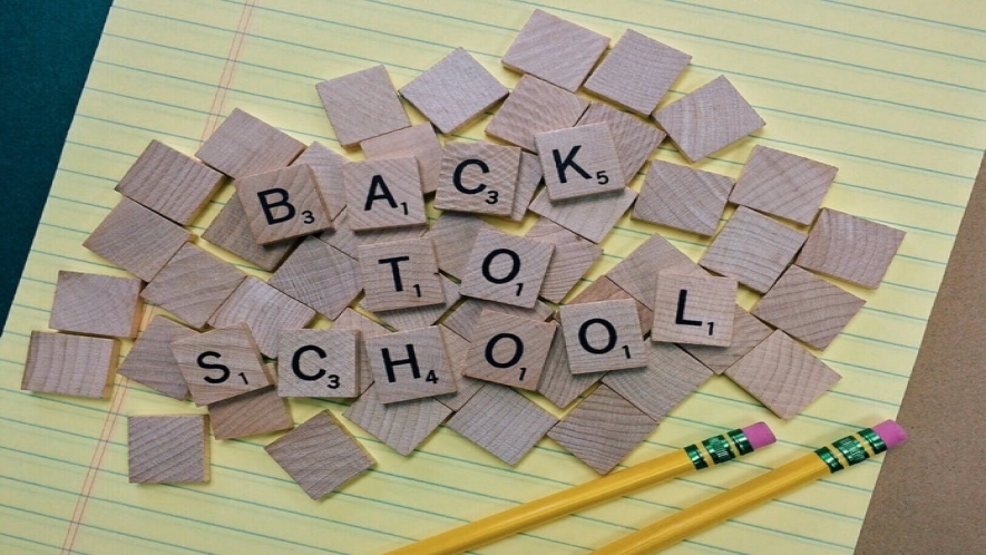 A photograph of scrabble tiles spelling out “back to school” on top of a yellow notepad.
