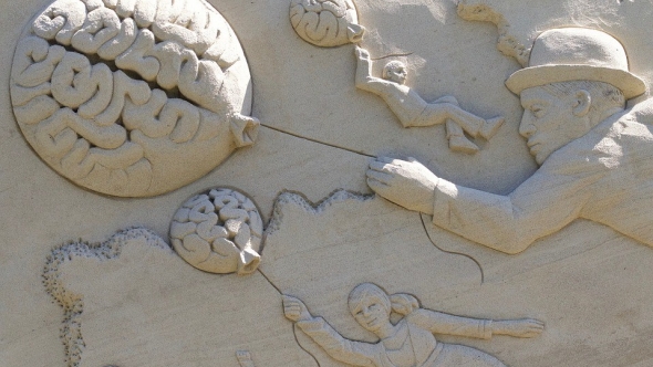 A photo of a sculpture with people flying away on balloons shaped like brains. 